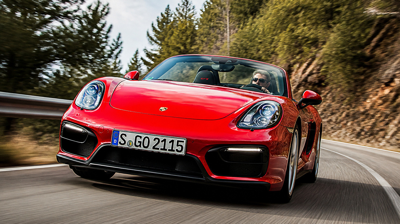 Carro esportivo vermelho Porsche conversível dirigindo em estrada sinuosa cercada por árvores.
