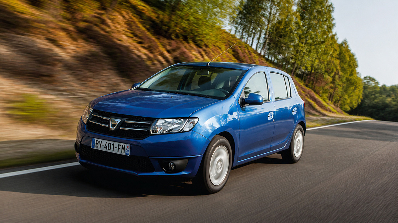 Carro azul modelo hatchback circulando em estrada asfaltada com árvores ao fundo.