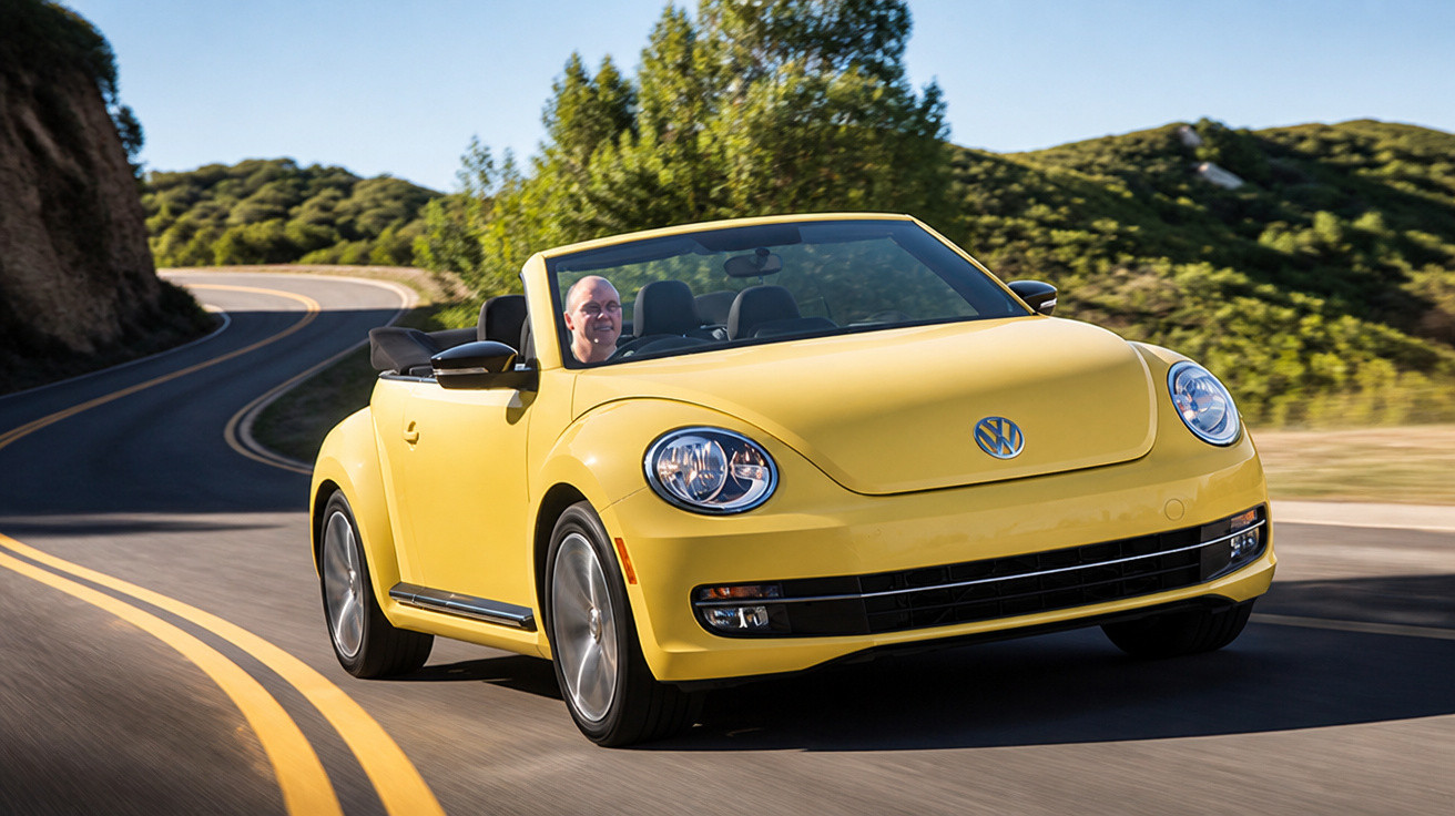 Carro conversível amarelo Volkswagen trafegando em estrada sinuosa com motorista ao volante em dia ensolarado.