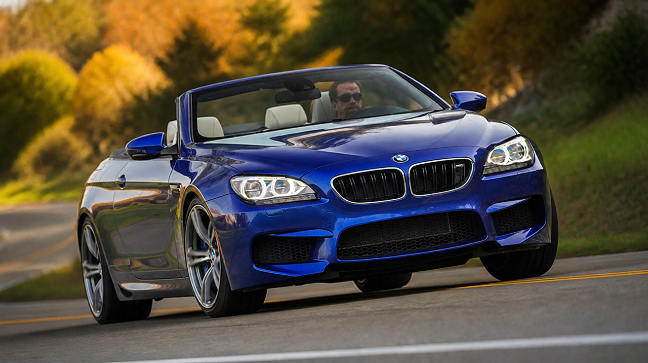 Carro conversível azul BMW em movimento em estrada com motorista usando óculos escuros.