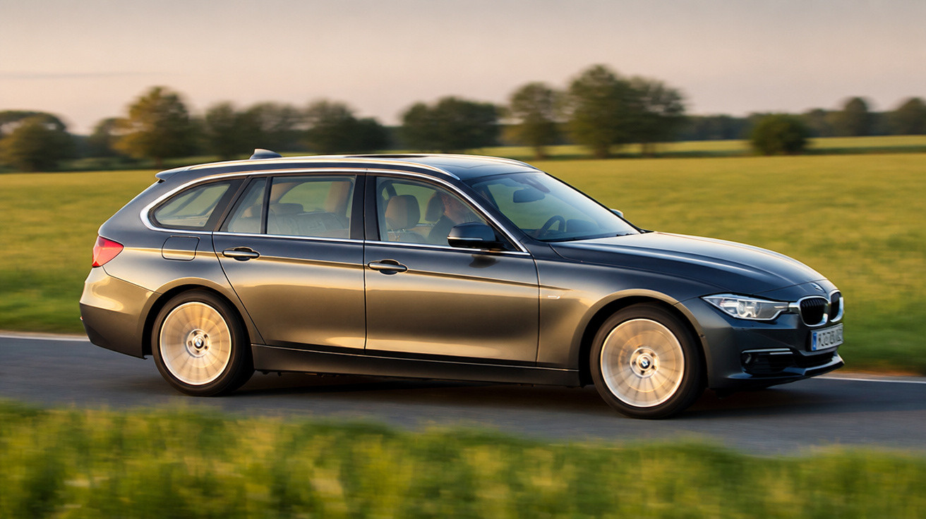 Carro BMW cinza modelo perua em movimento em estrada com campo verde ao fundo.