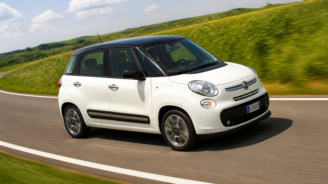 Carro branco com teto preto modelo hatchback Fiat 500L rodando em estrada asfaltada com vegetação ao fundo.