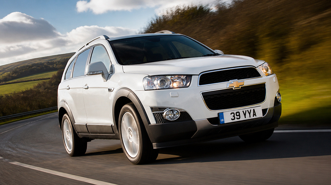 SUV branco Chevrolet em movimento em estrada curva com vegetação e céu nublado ao fundo.