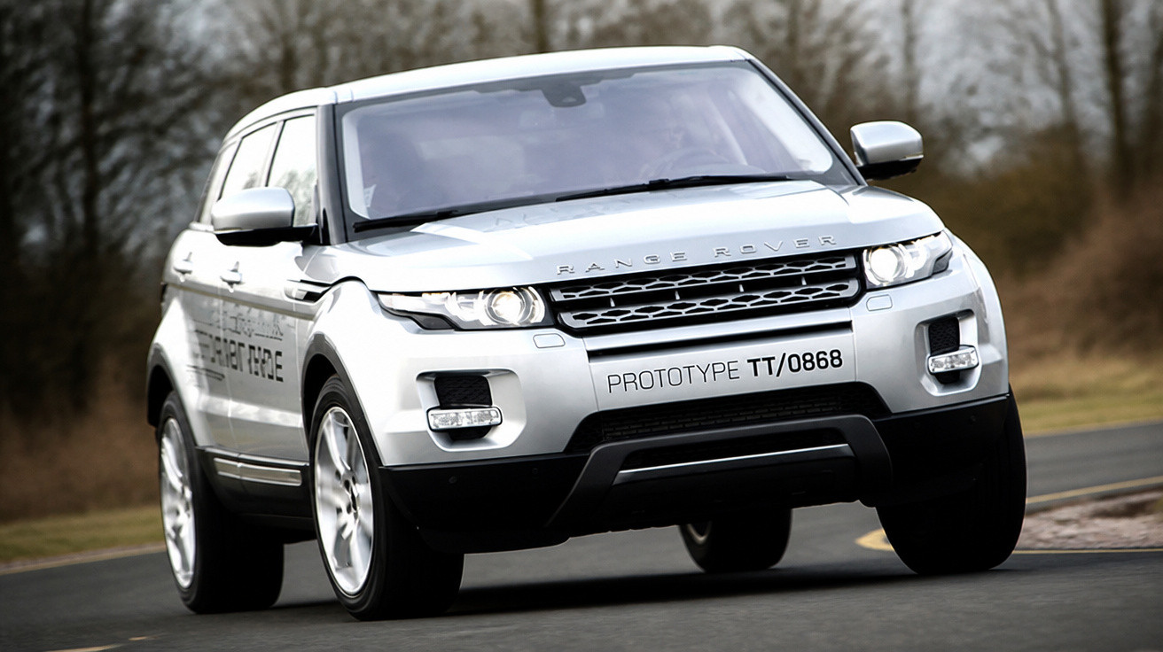 SUV branco Range Rover em curva fechada em estrada asfaltada com árvores ao fundo.
