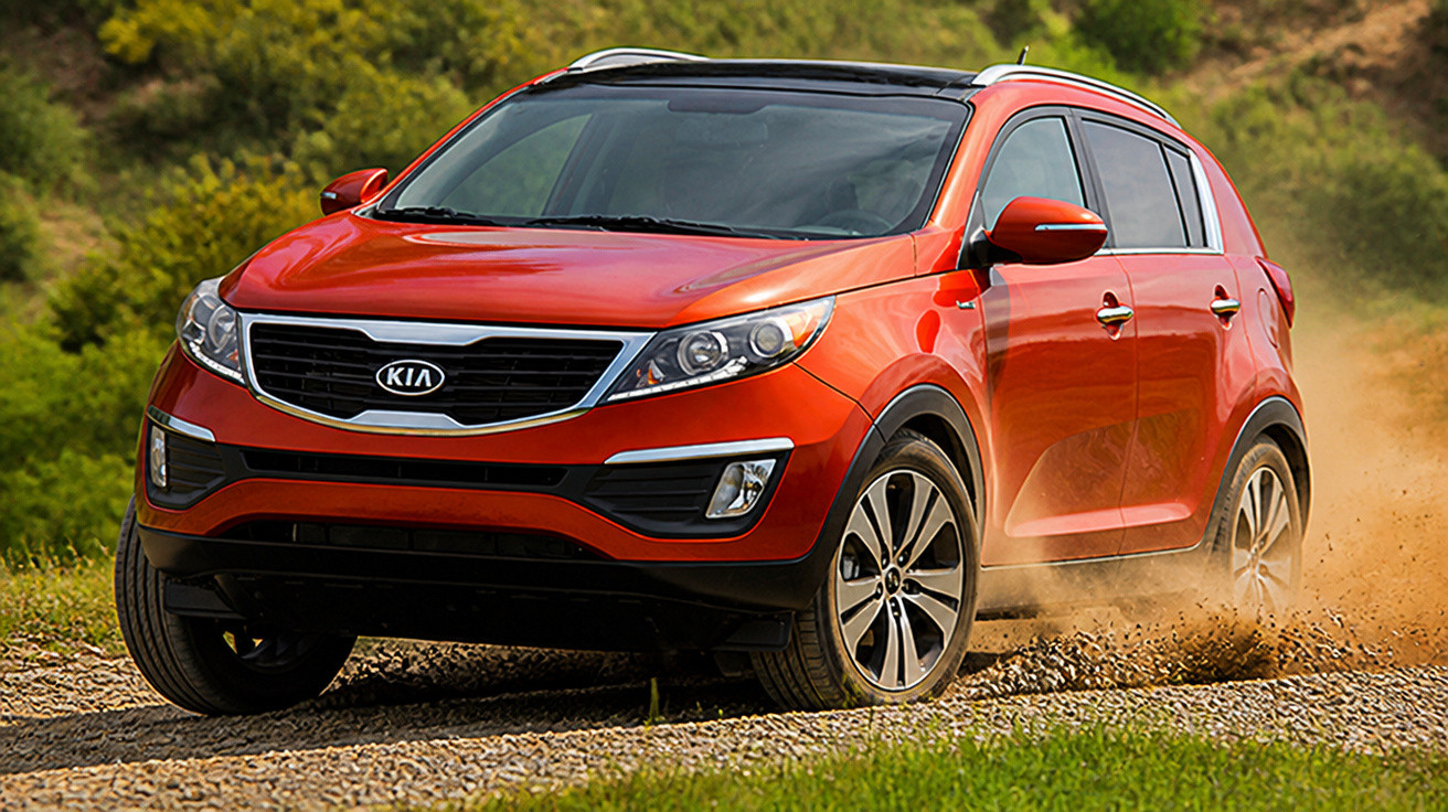 Carro SUV vermelho Kia em estrada de terra com poeira ao fundo e vegetação verde.